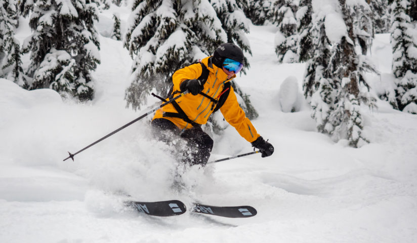 Skiier in a yellow jacket skiing past snowy trees