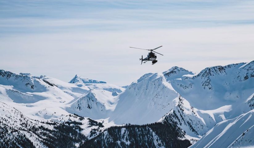 A helicopter flies above a snowy mountain range