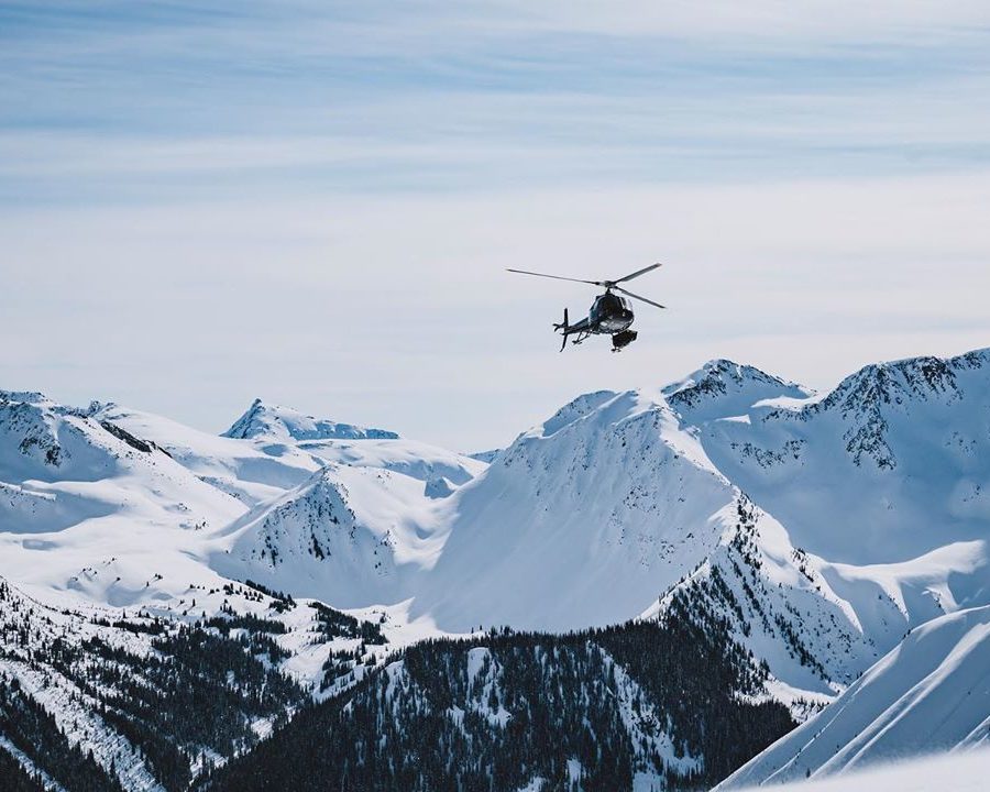 A helicopter flies above a snowy mountain range