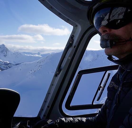 A helicopter pilot flying with a view of snowy mountains through the windows