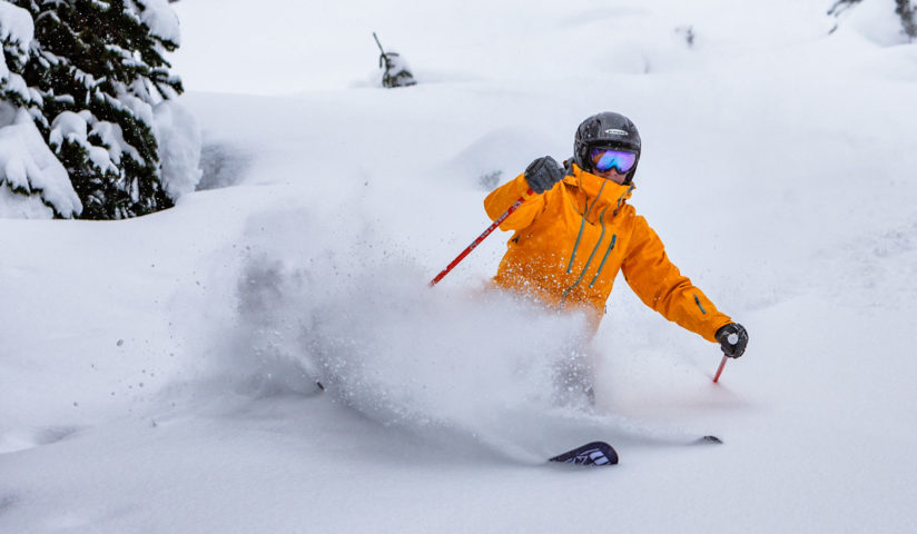 Action shot of a skiier in an orange jacket kicking up powder