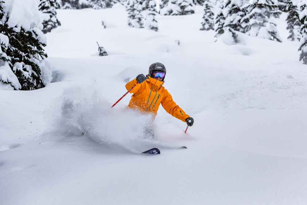 Action shot of a skiier in an orange jacket kicking up powder