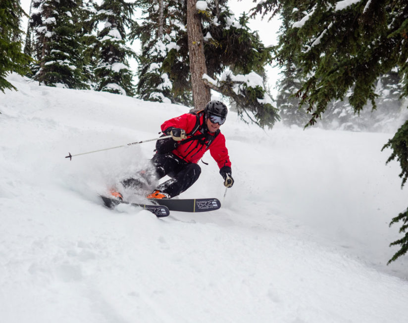 Action shot of a skiier in a red jacket skiing past trees