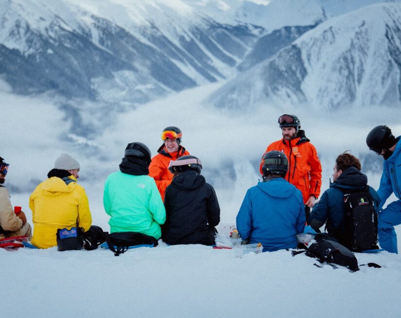 Group of skiers and guides sharing a mountaintop meal during a heliskiing adventure