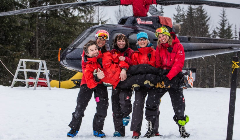 A group of skiiers smile in front of a helicopter