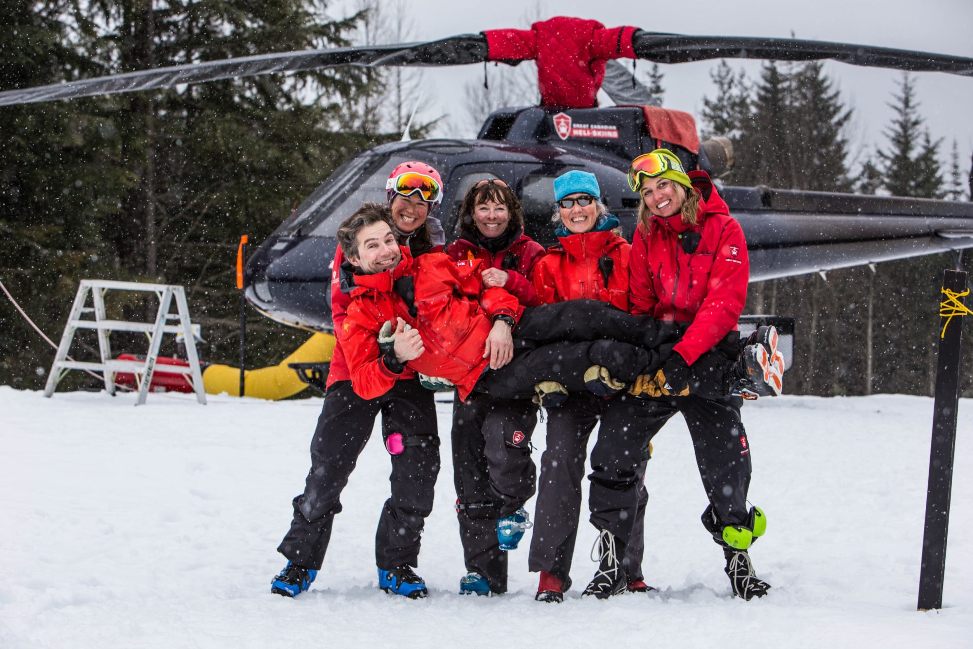 A group of skiiers smile in front of a helicopter