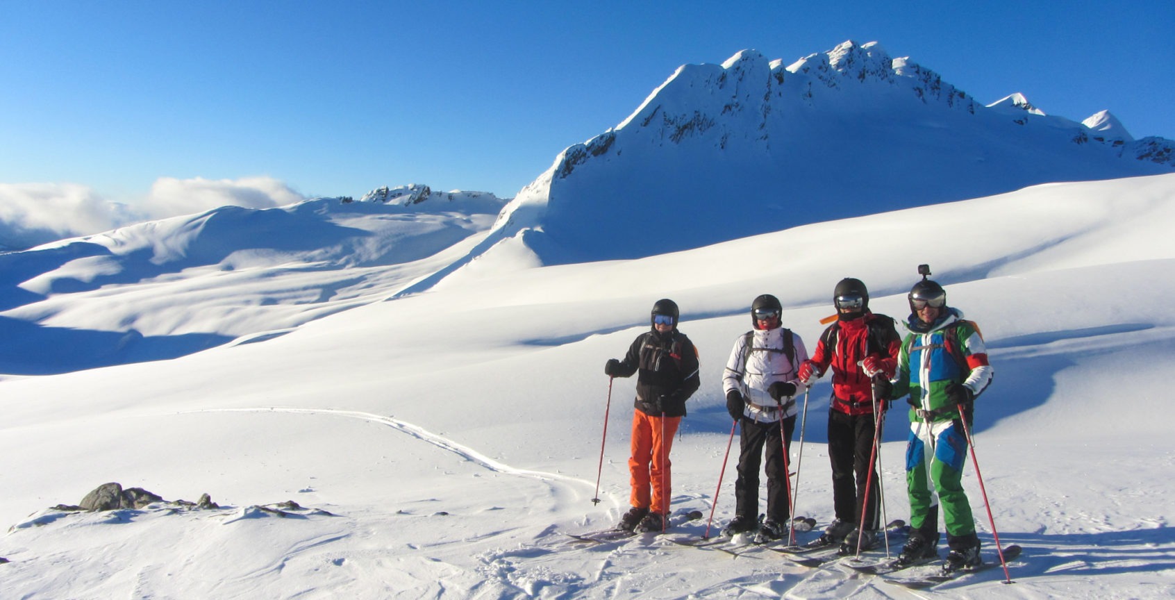 4 skiiers stand at the top of a run in the sunshine