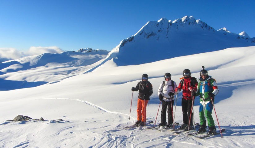 4 skiiers stand at the top of a run in the sunshine