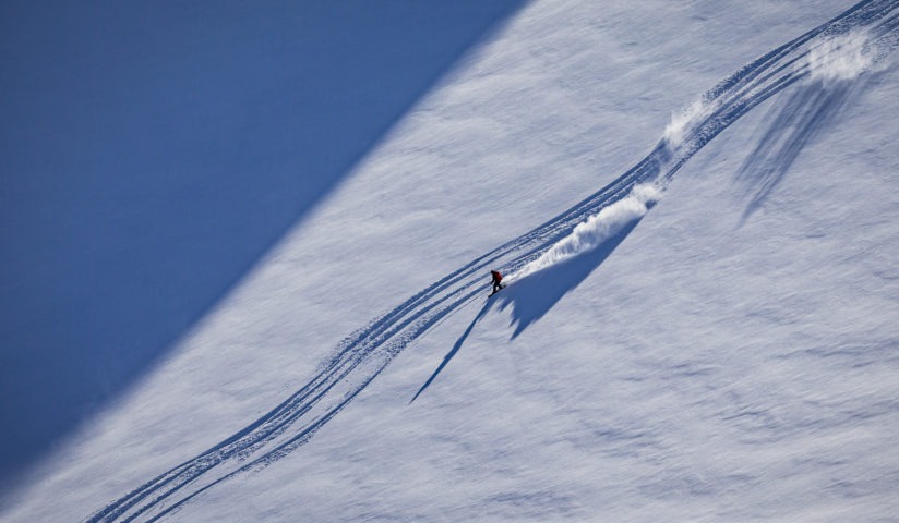 Snowboarder heliskiing powder in alpine terrain