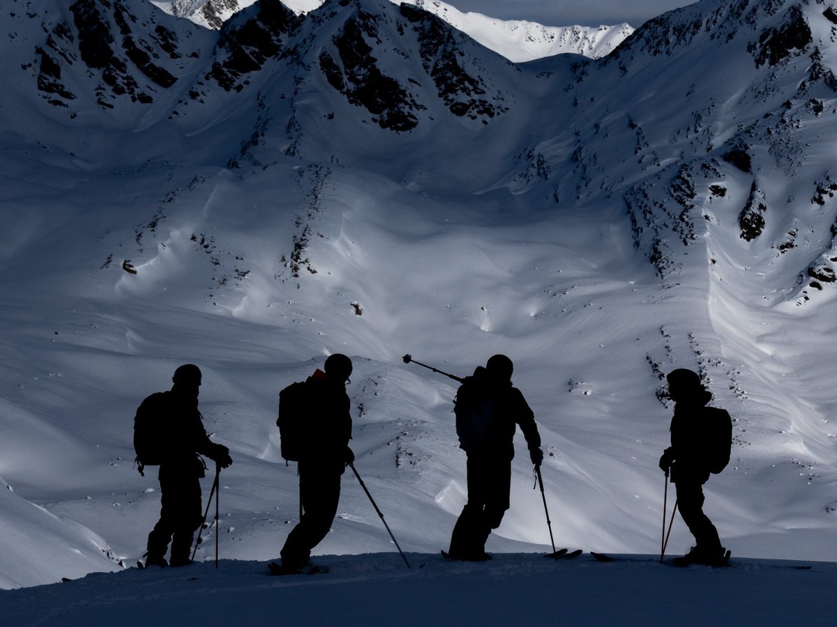 A small group of heliskiers silhouetted against the alpine terrain during a guided descent in Canada