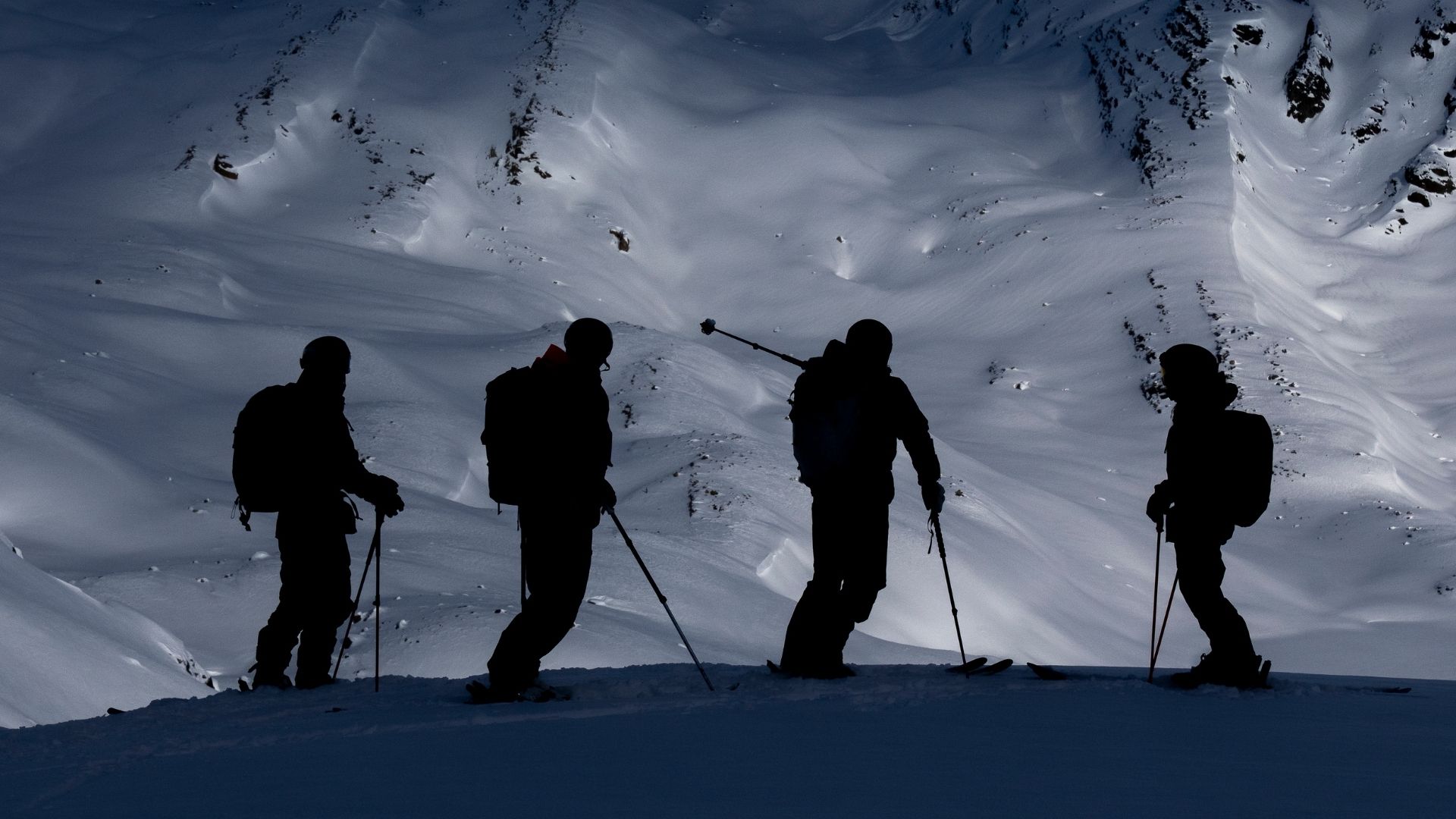 Four heliskiers silhouetted against a backdrop of dramatic peaks in British Columbia
