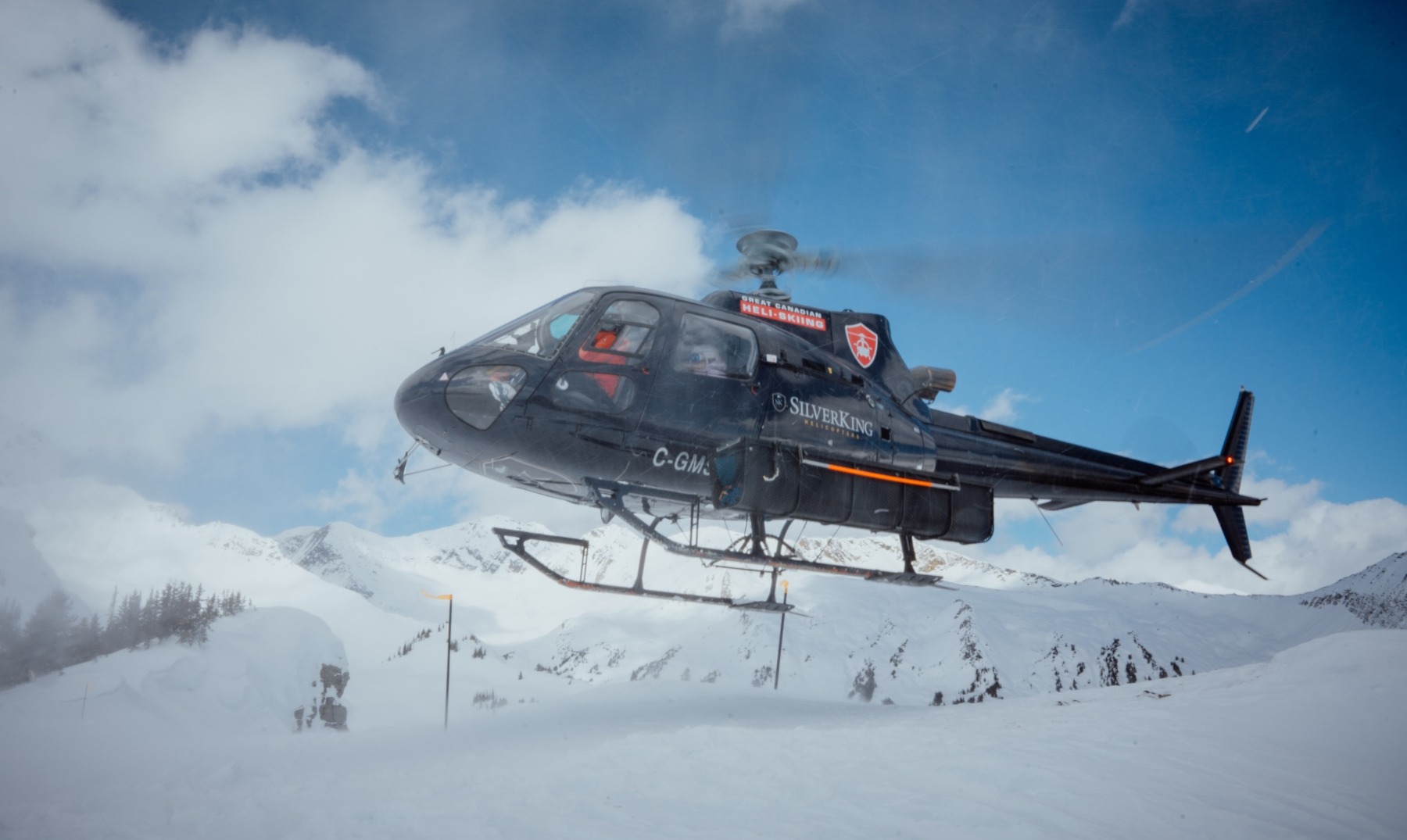 Helicopter lifting off in snowy Canadian mountains during a heliskiing operation