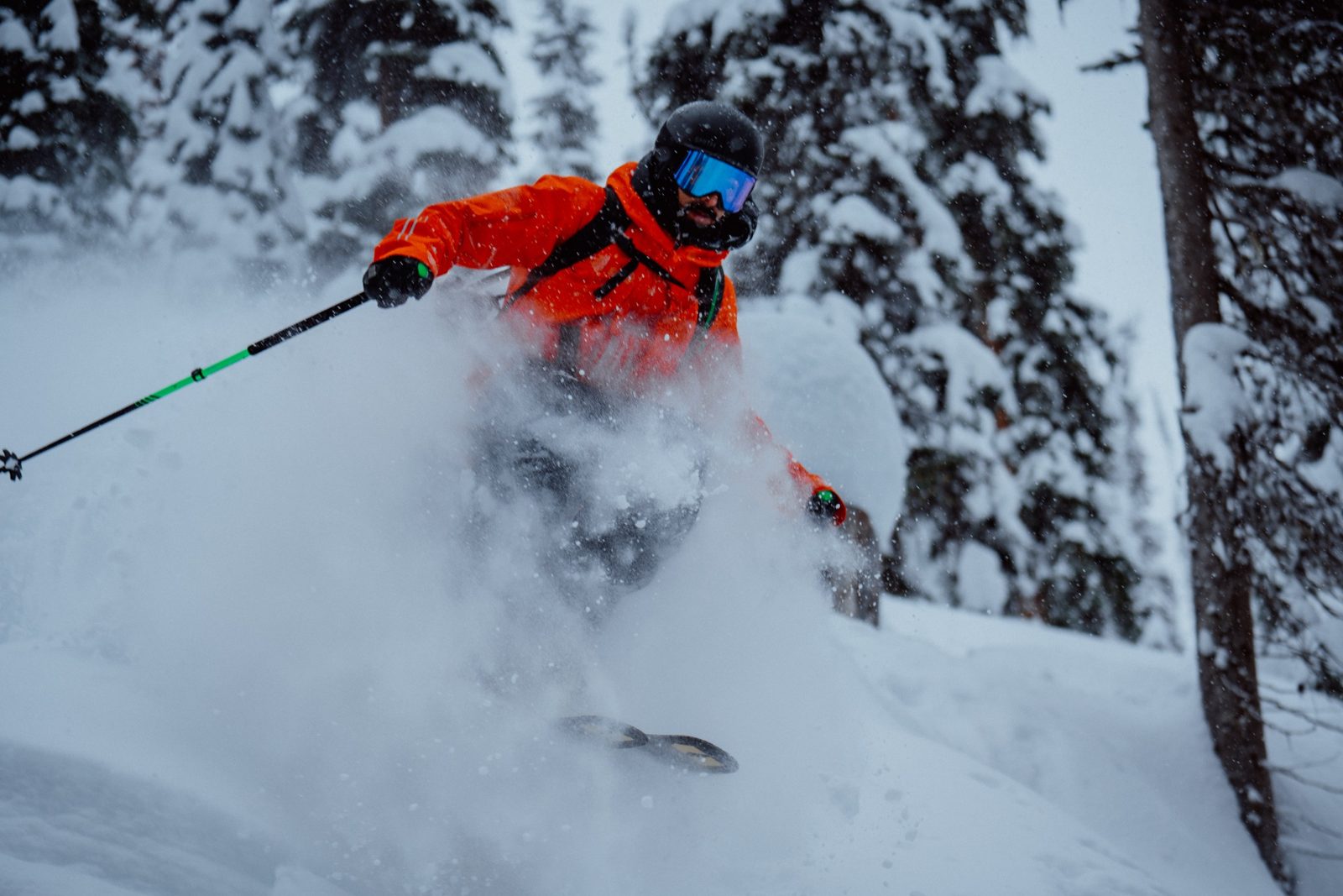 Heliskier in bright orange jacket carving through deep powder snow
