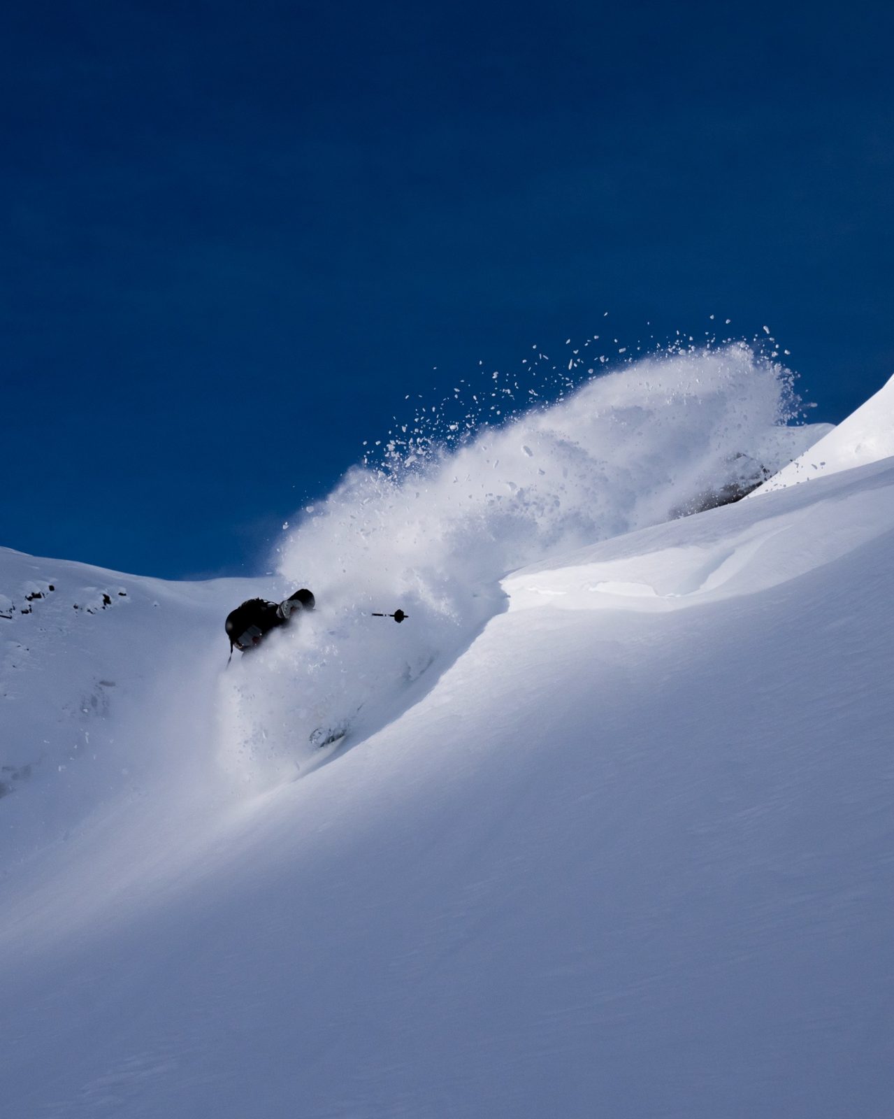 Skier making a powerful turn on a steep slope with a dramatic spray of powder