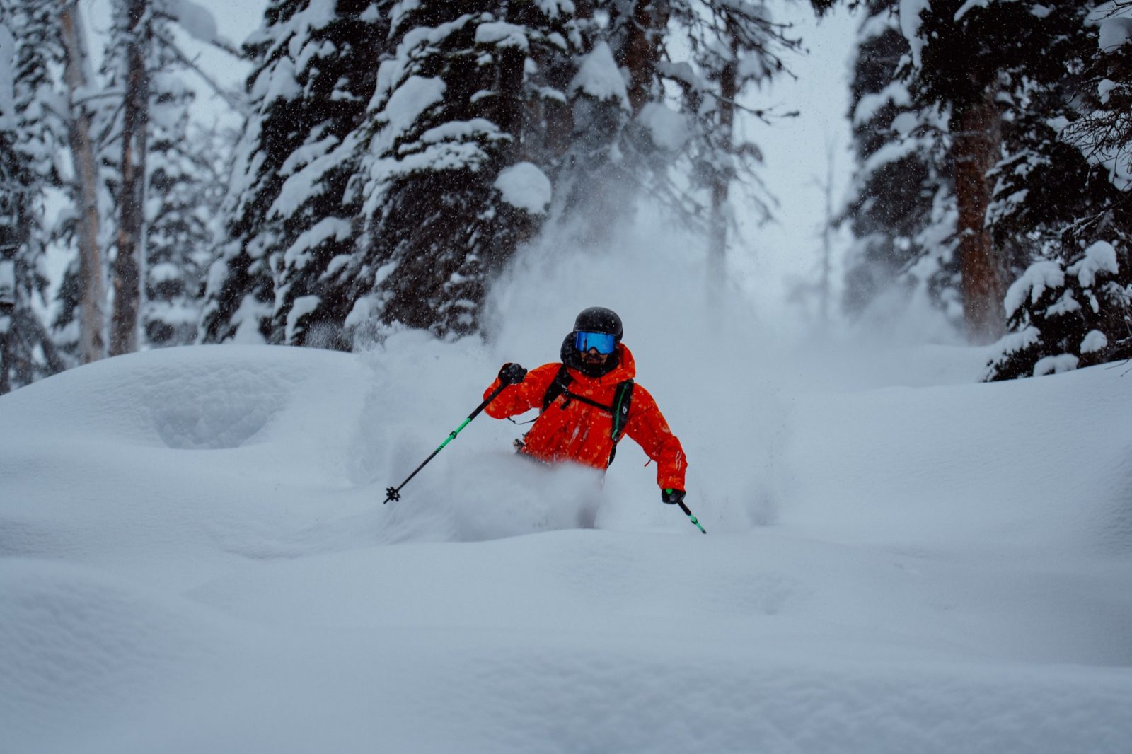Heliskier in bright orange jacket skiing through deep untouched powder